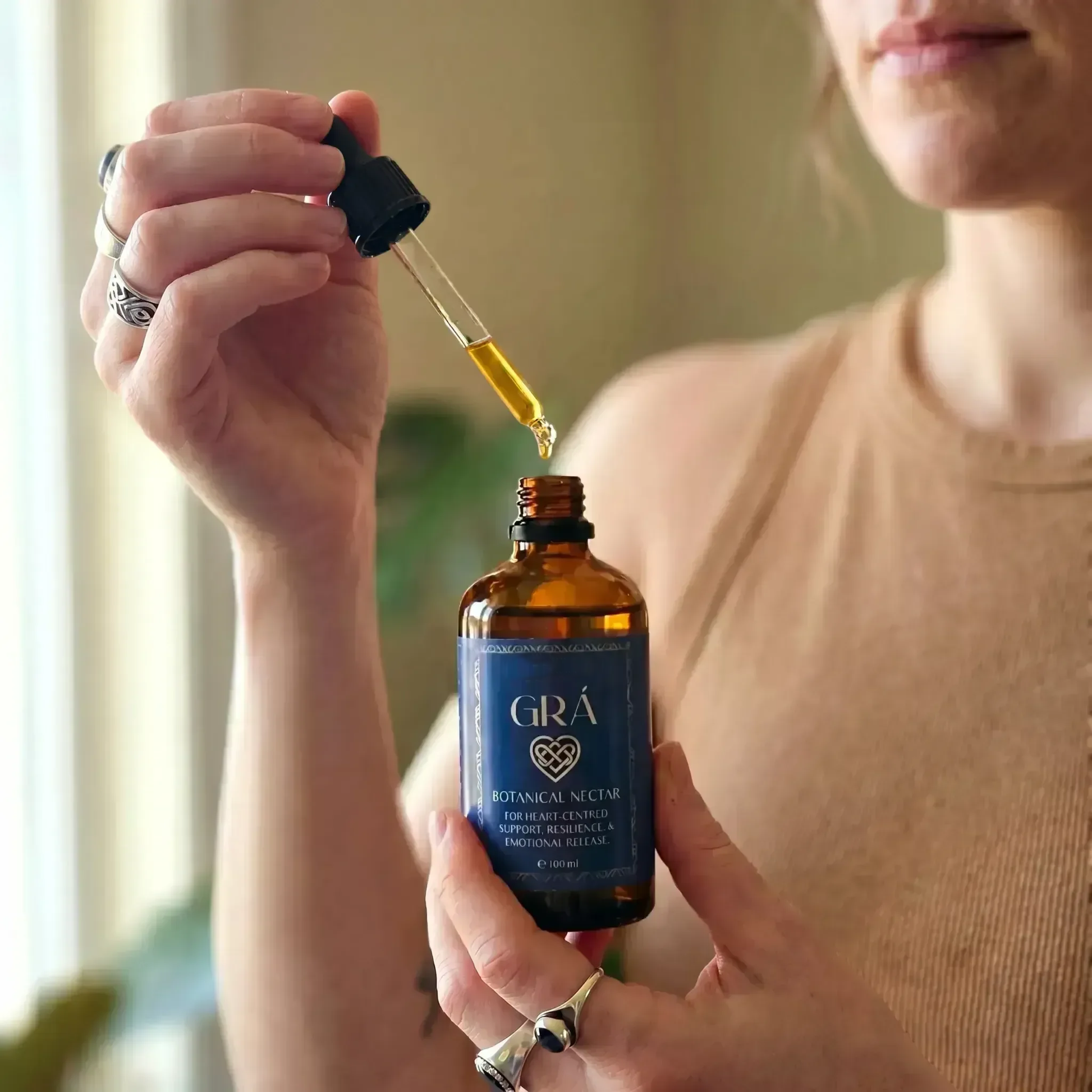 Woman holding a bottle of Grá botanical tincture with a dropper.